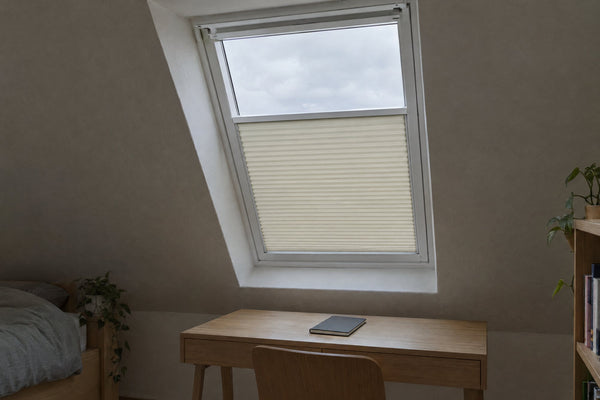 Dachfenster mit verspanntem Plissee in seitlichen Führungsschienen über einem Schreibtisch